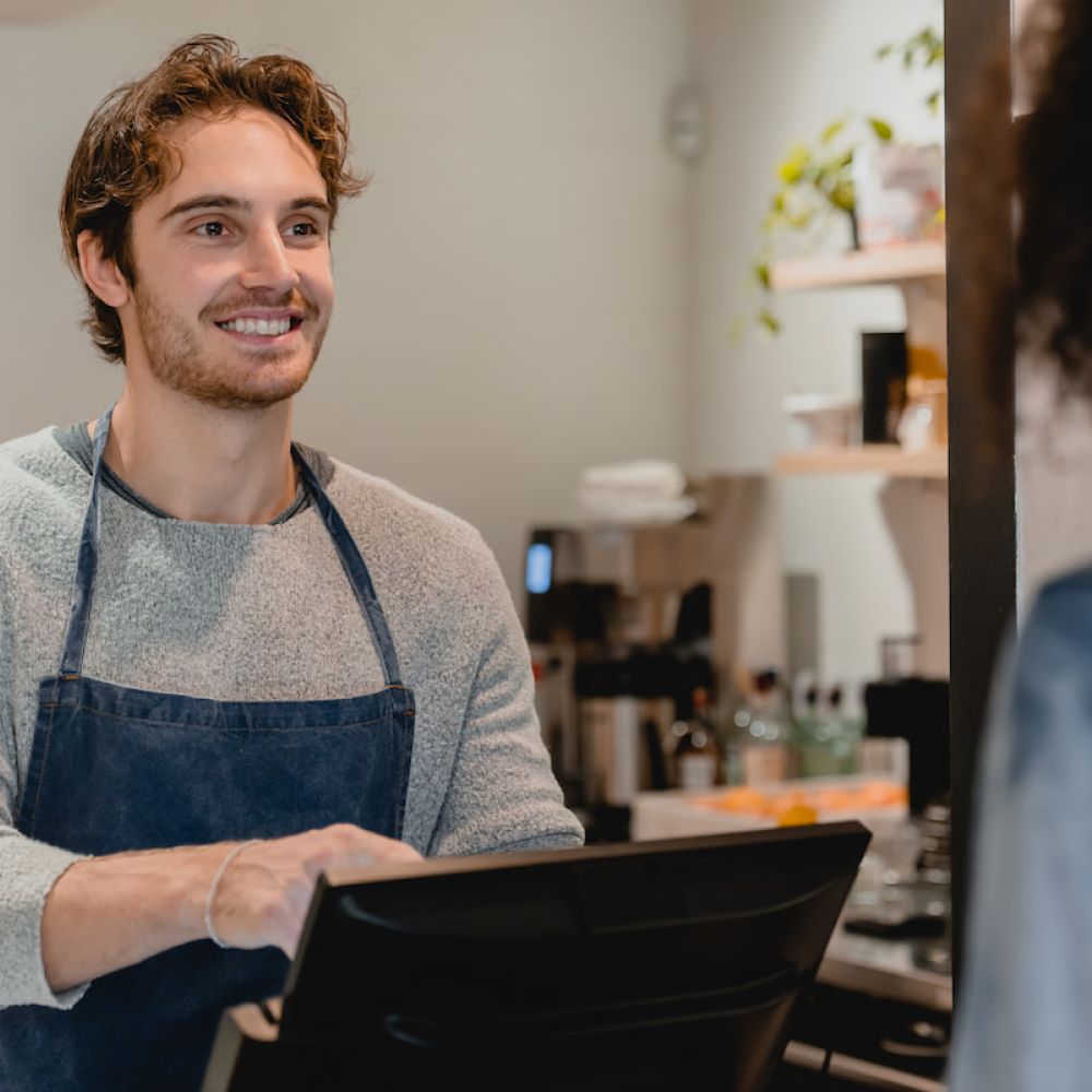 Un jeune et séduisant serveur attend les commandes près de la caisse de la cafétéria.